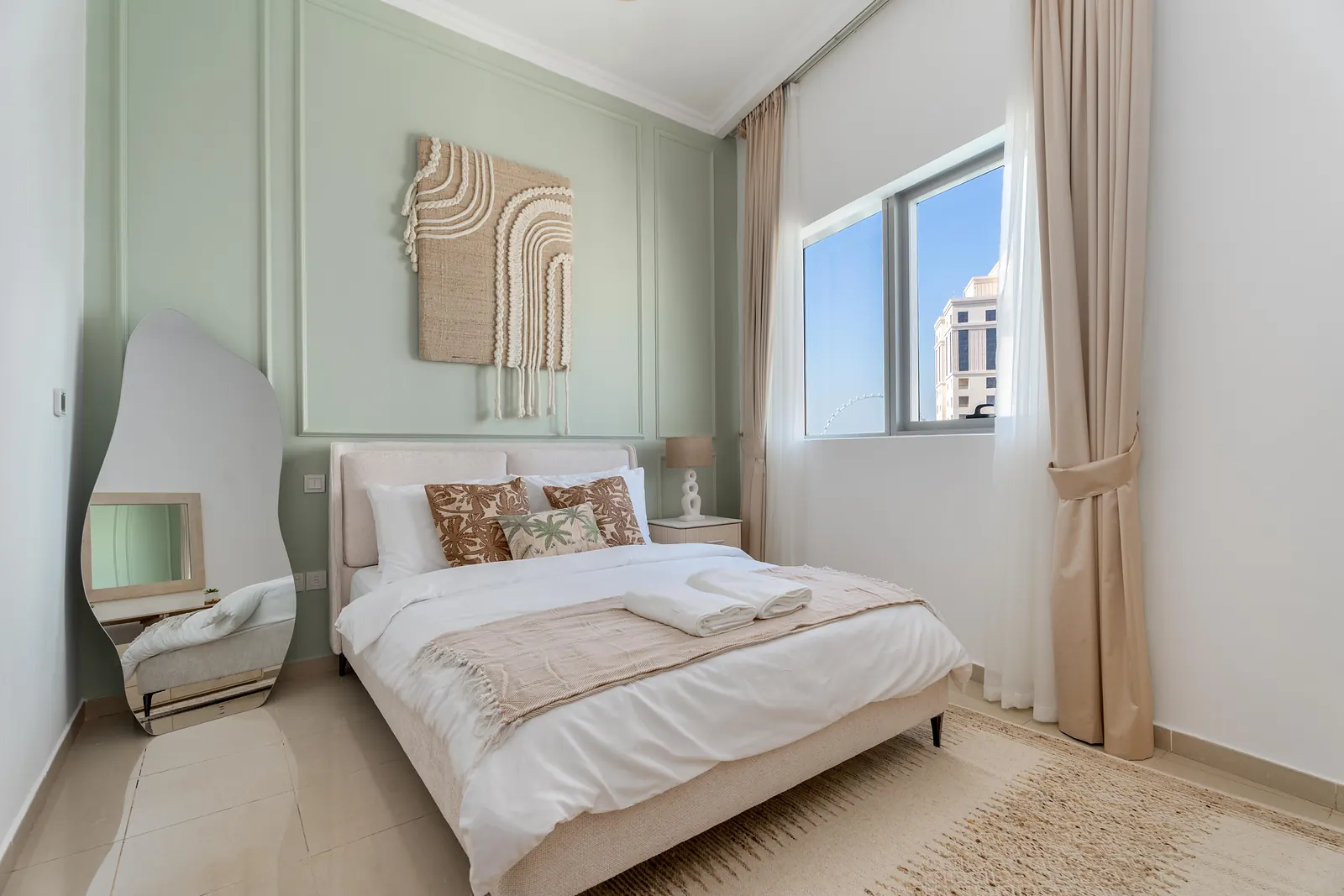 Bedroom with sage-green moulding, macramé art and a sculpted floor mirror