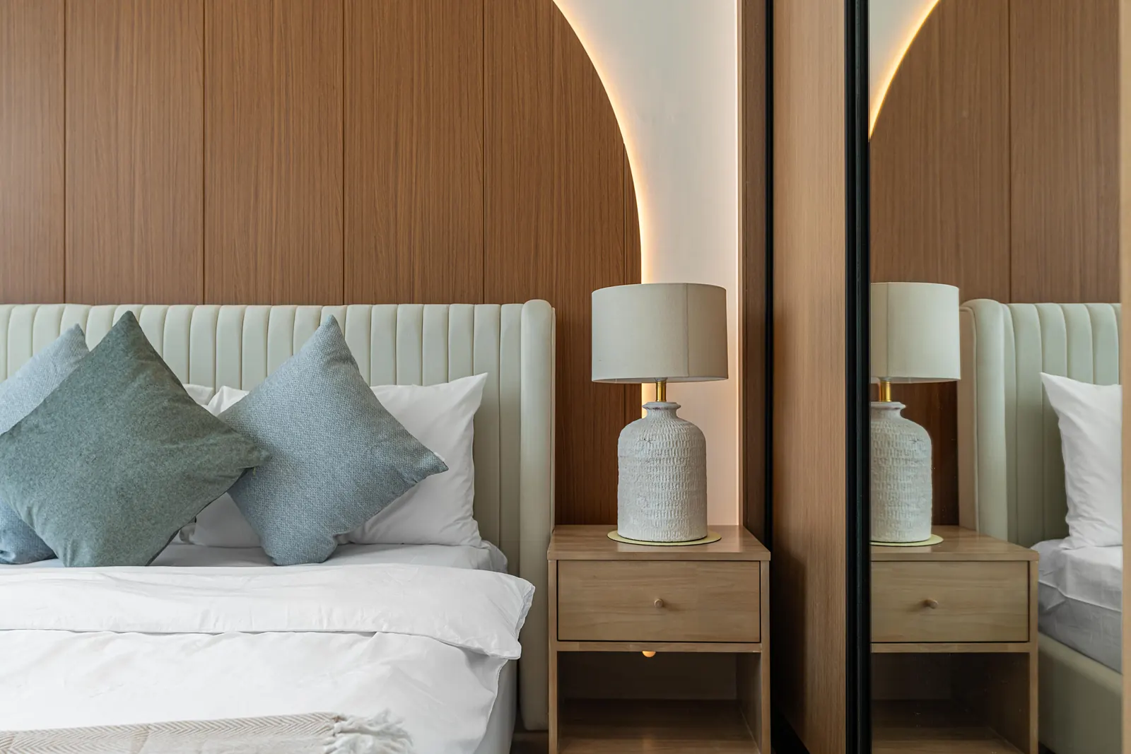 Close-up of the timber arch and its hidden LED glow beside a bedside table and ceramic lamp