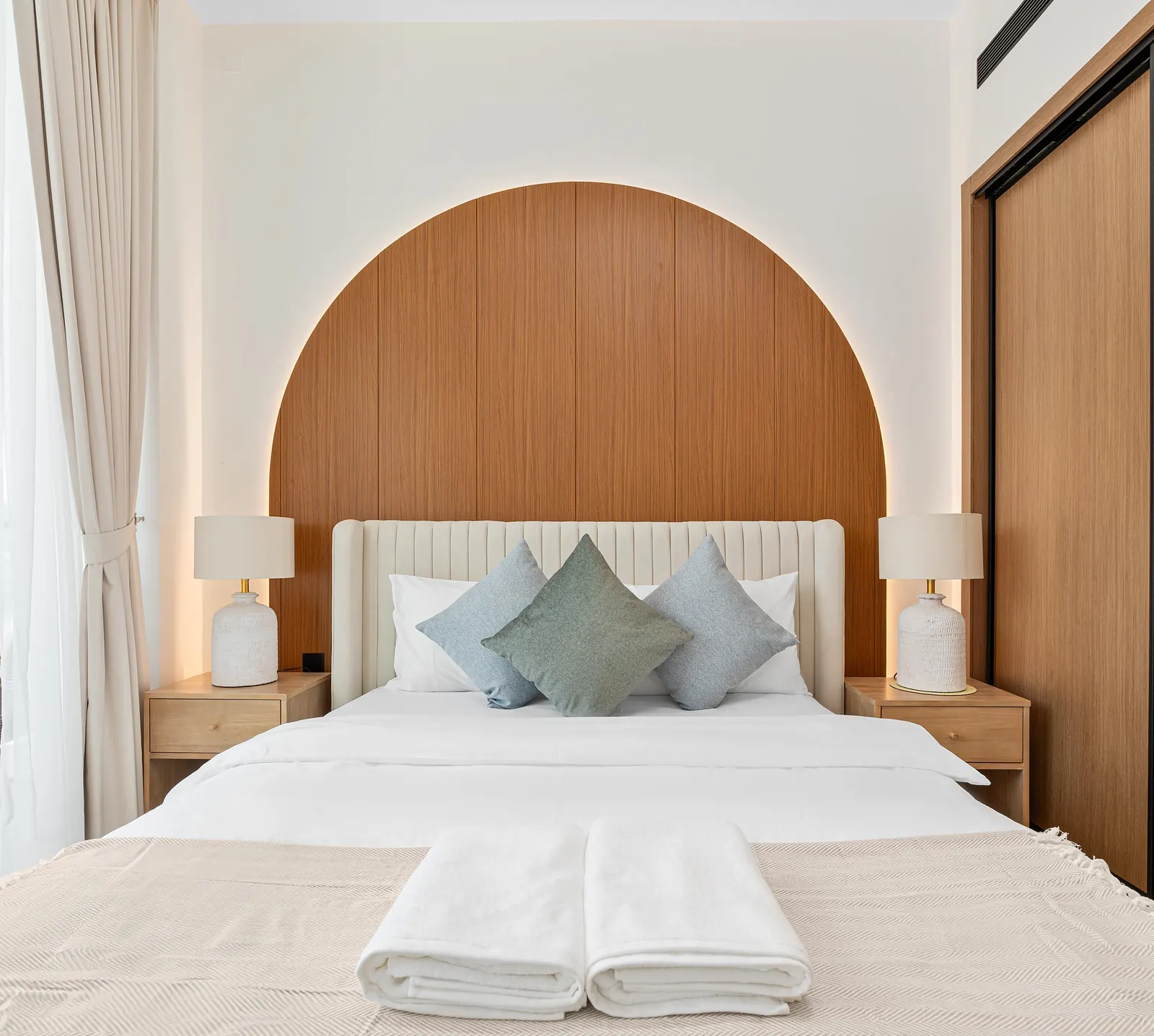 Main bedroom with an arched timber headboard wall lit from behind, a channel-tufted bed and matching bedside lamps