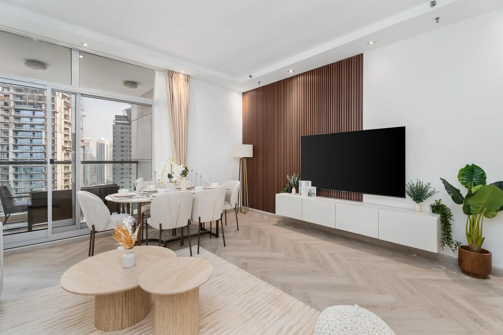 Living and dining room with a walnut slatted TV wall, round travertine-look coffee tables and a dining table for six